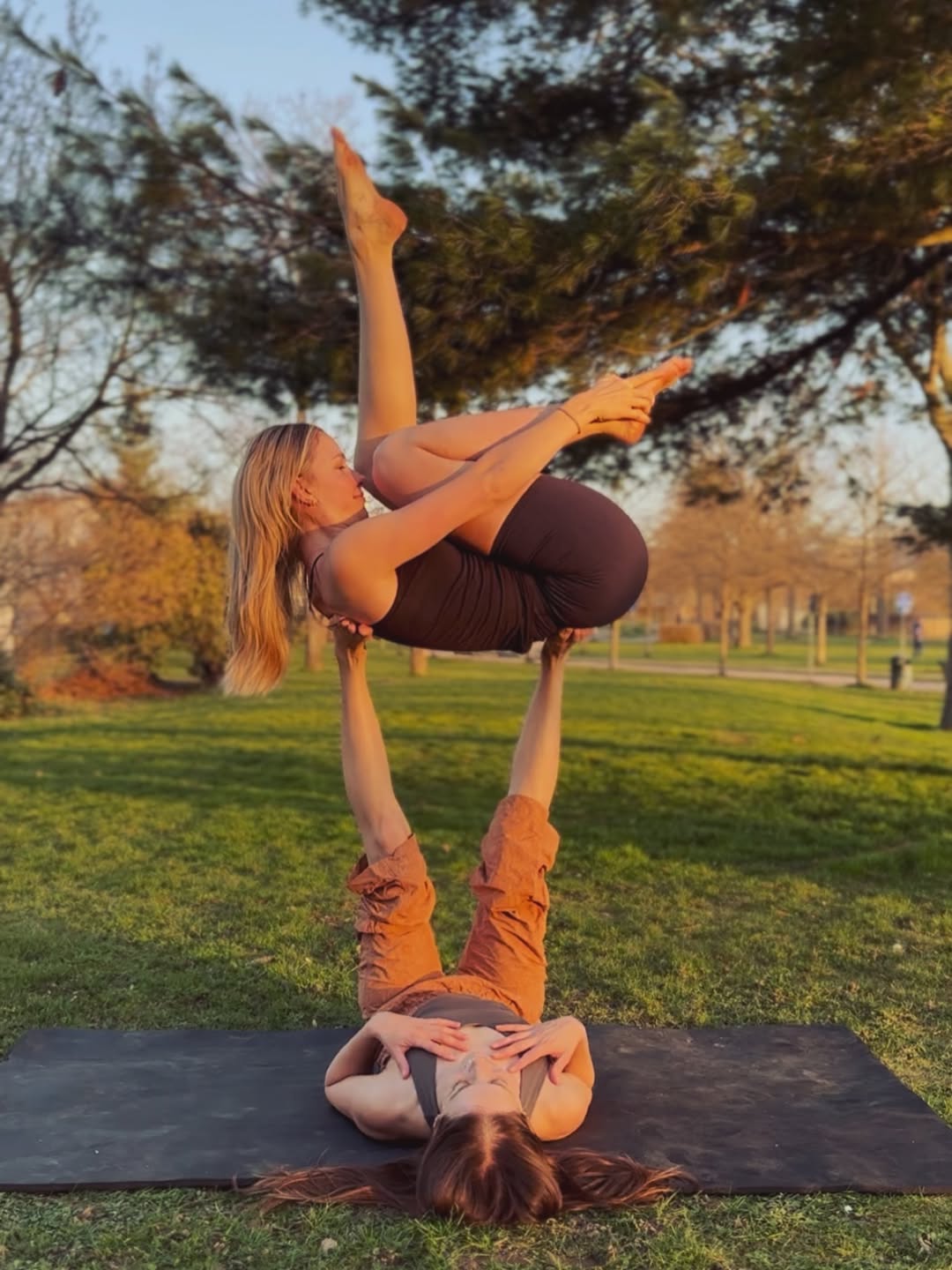 Zwei Übende in einer fliegenden AcroYoga-Pose im goldenen Abendlicht